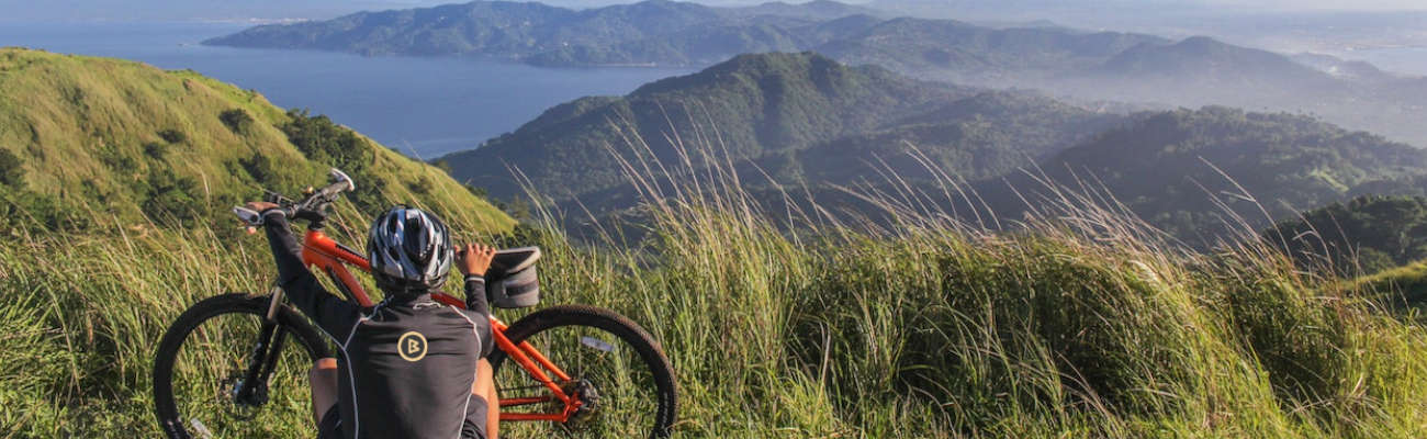 Imagem de um ciclista segurando uma bicicleta enquanto visualiza a paisagem de uma área montanhosa. A imagem está ilustrando o texto Café e ciclismo: entenda a relação do grão com o esporte e aproveite a energia da bebida para melhorar o seu desempenho